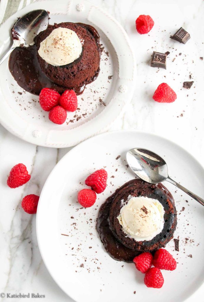 Overhead view of two chocolate lava cakes on a white marble surface, with molten chocolate oozing out of each