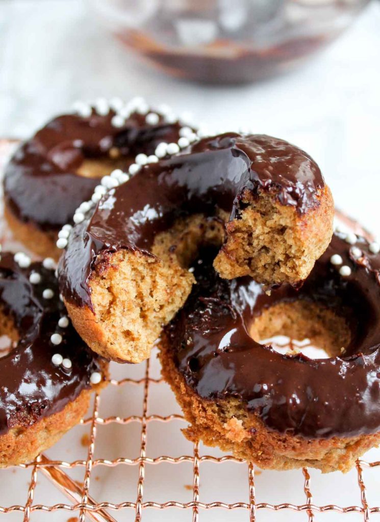 A stack of Baked Banana Donuts with Dark Chocolate Glaze with a bite taken out of one of the donuts