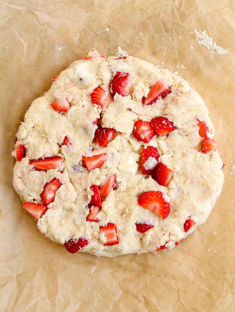 Scone dough arranged in a disk on parchment with strawberry chunks throughout
