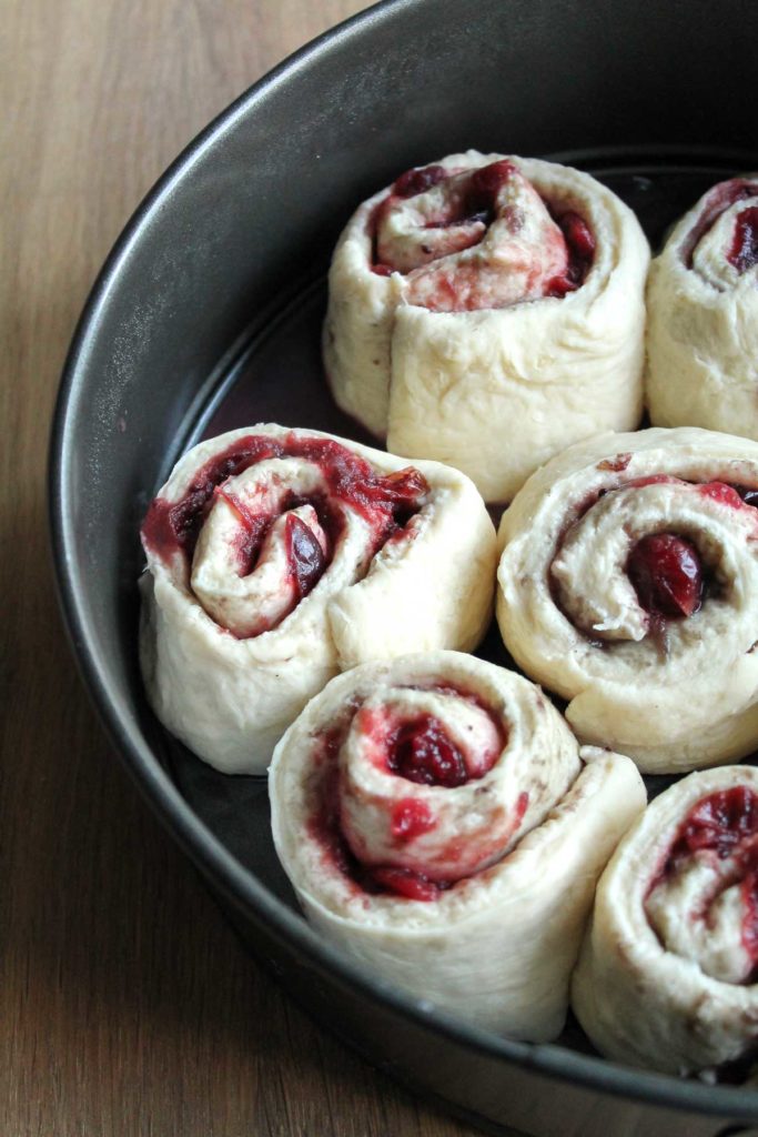 rolls of sweet bread dough with leftover cranberry sauce as the filling in a pan and ready to rise before baking