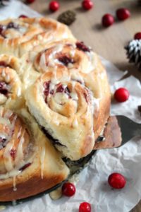 a sweet roll with leftover cranberry sauce filling and orange glaze being lifted out of the pan with a spatula