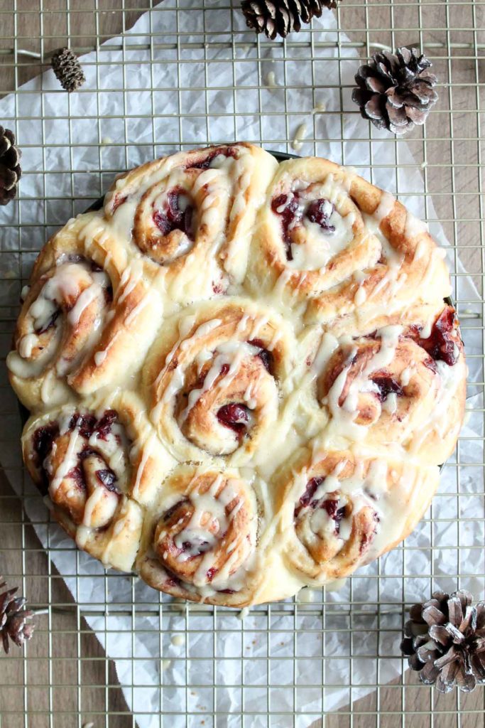 Finished pan of sweet rolls using leftover cranberry sauce as the filling, glazed with an orange glaze, sitting on a wire rack