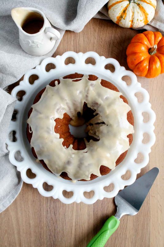 an overhead view of the finished cake on a serving plate with serving utensils and pumpkins