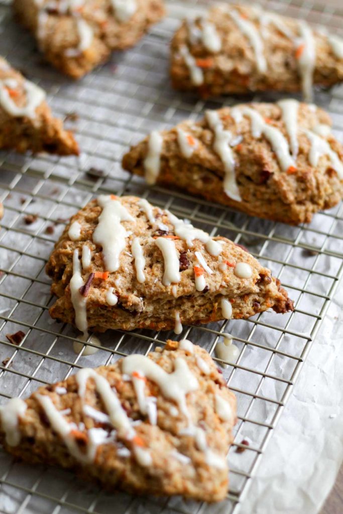 45 degree angle view of finished carrot cake scones with a cream cheese glaze on a wire rack, showing the layers of the scone and glaze drizzled on top