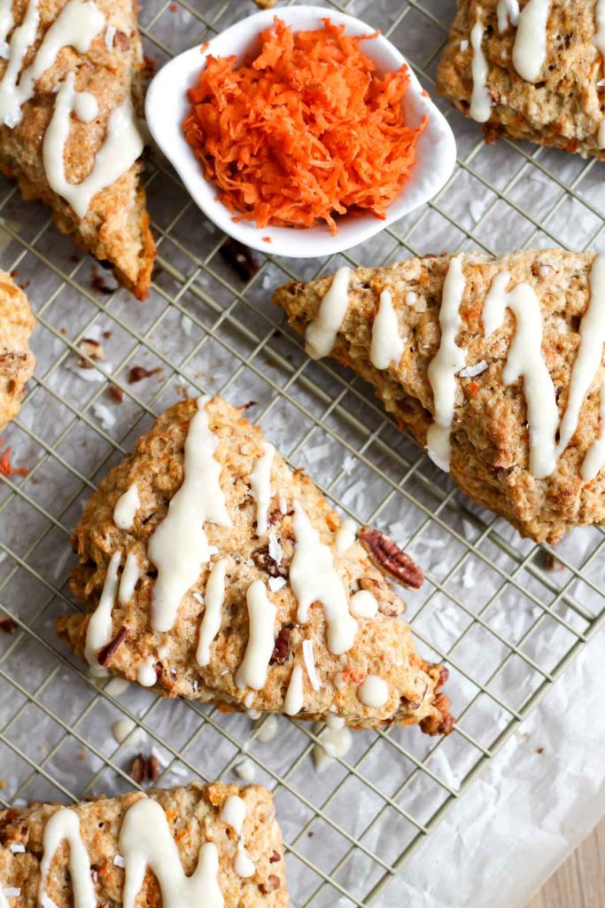 Overhead view of glazed Carrot Cake Scones on a wire rack with a bowl of shredded carrots