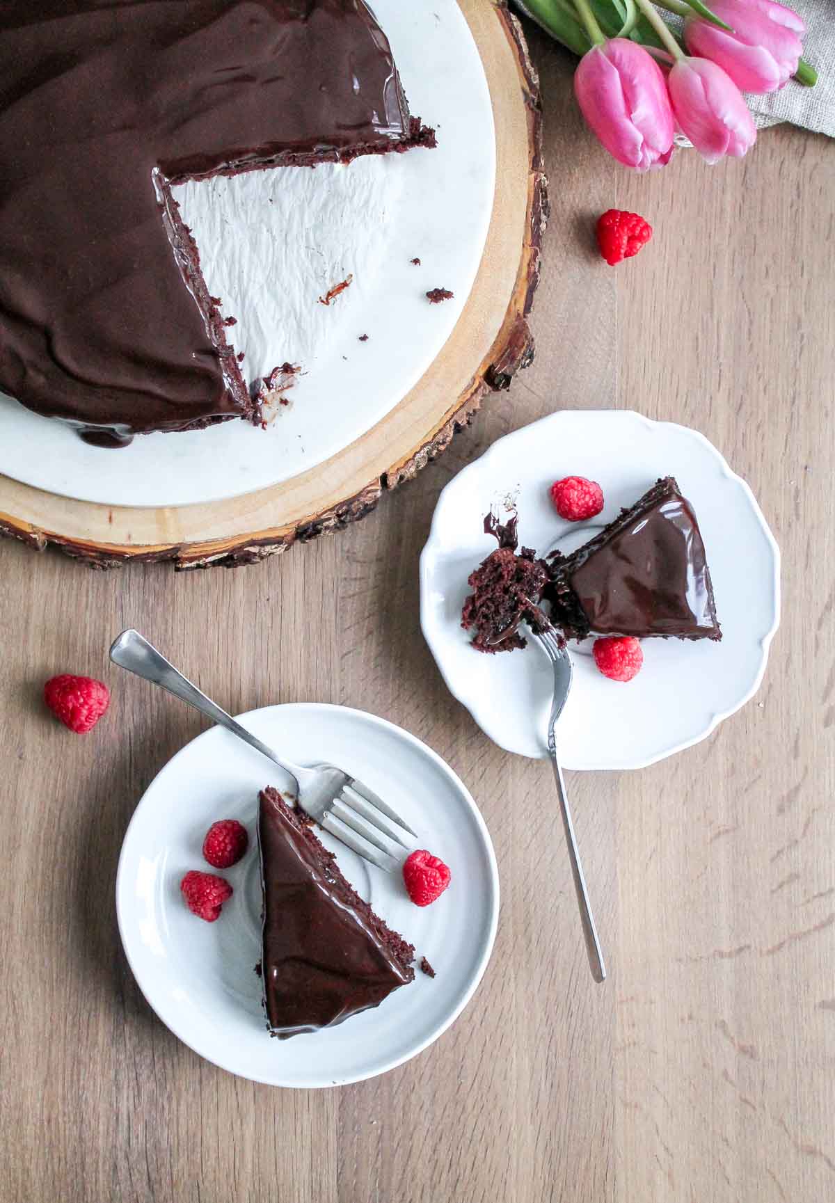 Overhead shot - Two slices of chocolate ganache cake with forks digging into them on a wooden table 