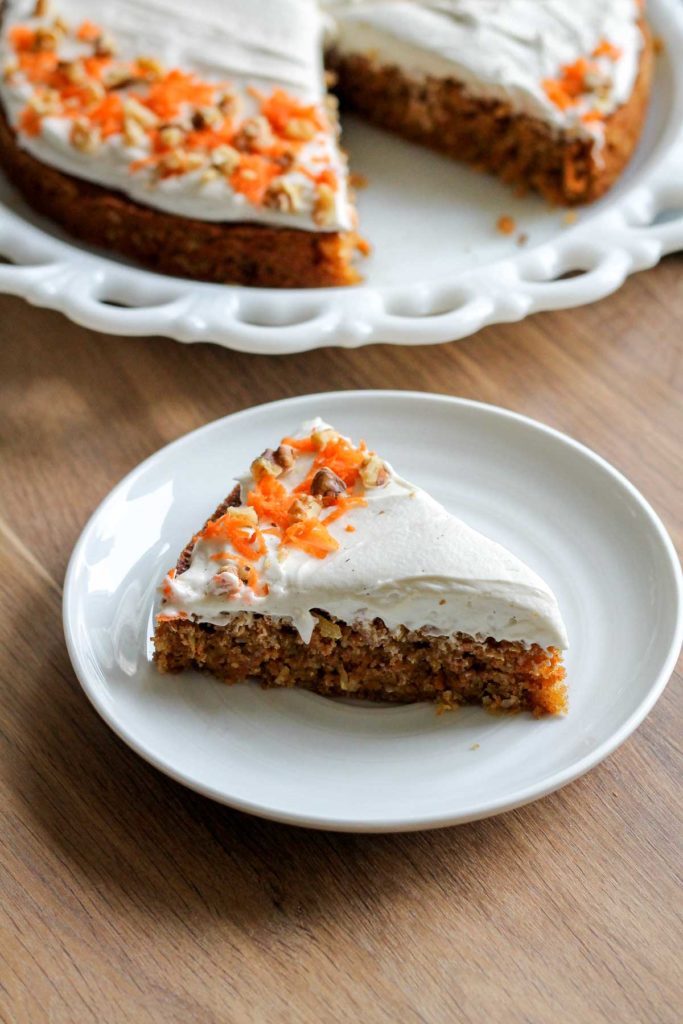 A slice of simple one Layer Carrot Cake with fluffy Cream Cheese Frosting, on a white plate and wood table