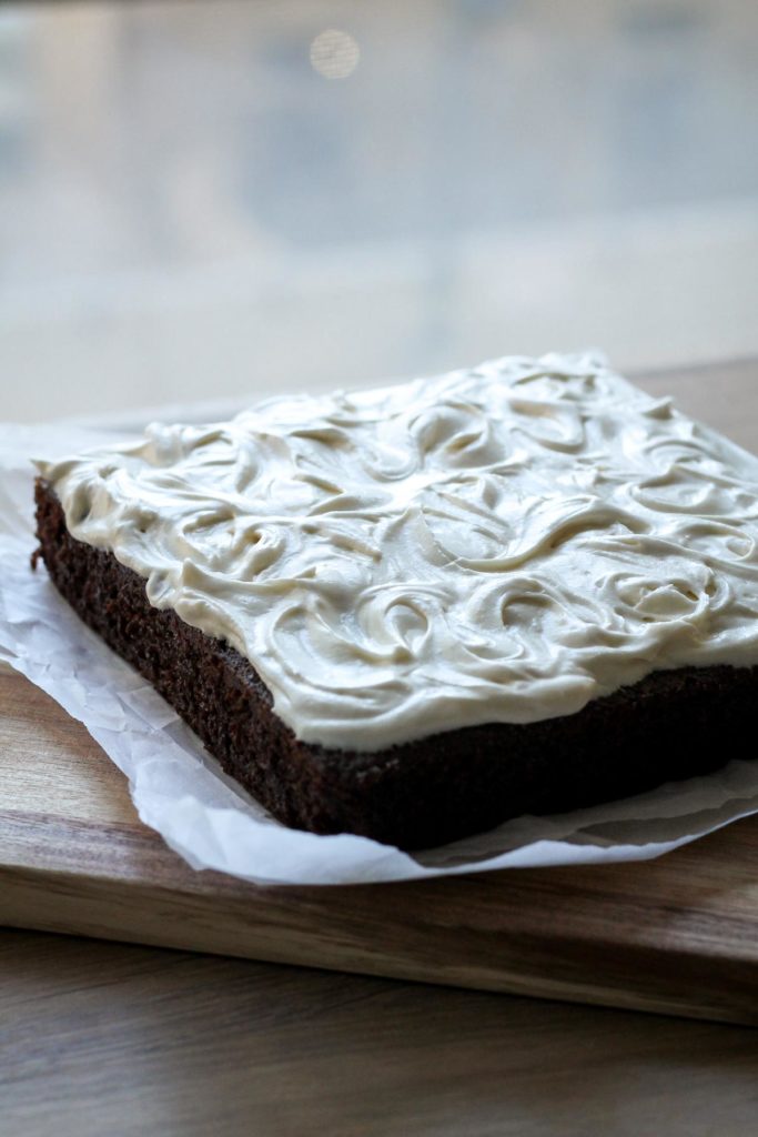 The finished frosted cake (swirls of frosting over top) on a cutting board in front of a window