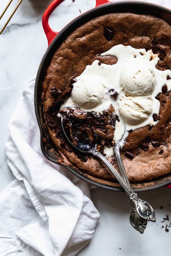 two spoons digging into the fudgy flourless almond butter brownies, showing the interior melty chocolate with ice cream mixing into it