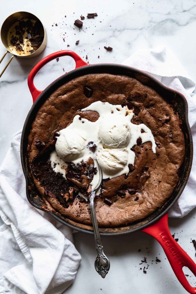 Overhead view of flourless Almond Butter Brownies in a red skillet with vanilla ice cream over top and a spoon taking a bite out of the fudgy and rich brownies that are completely flourless and gluten-free!