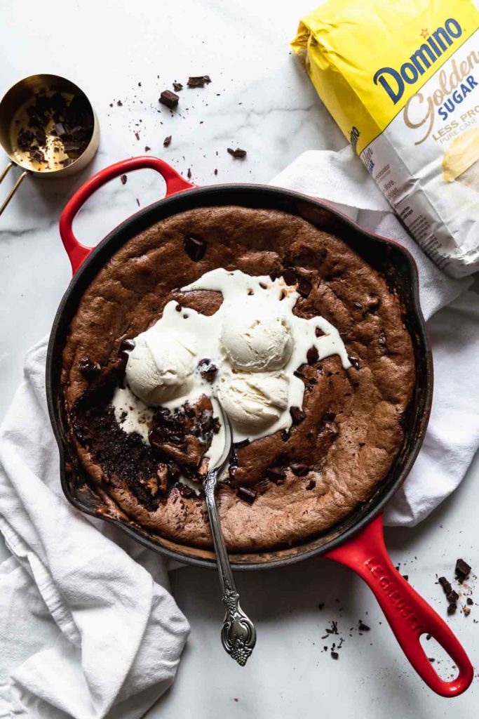 overhead view of almond butter brownies in a skillet on a white surface, with ice cream over top