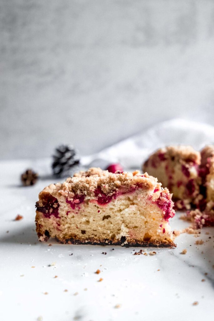 A cross section slice of cranberry crumb coffee cake on a white surface