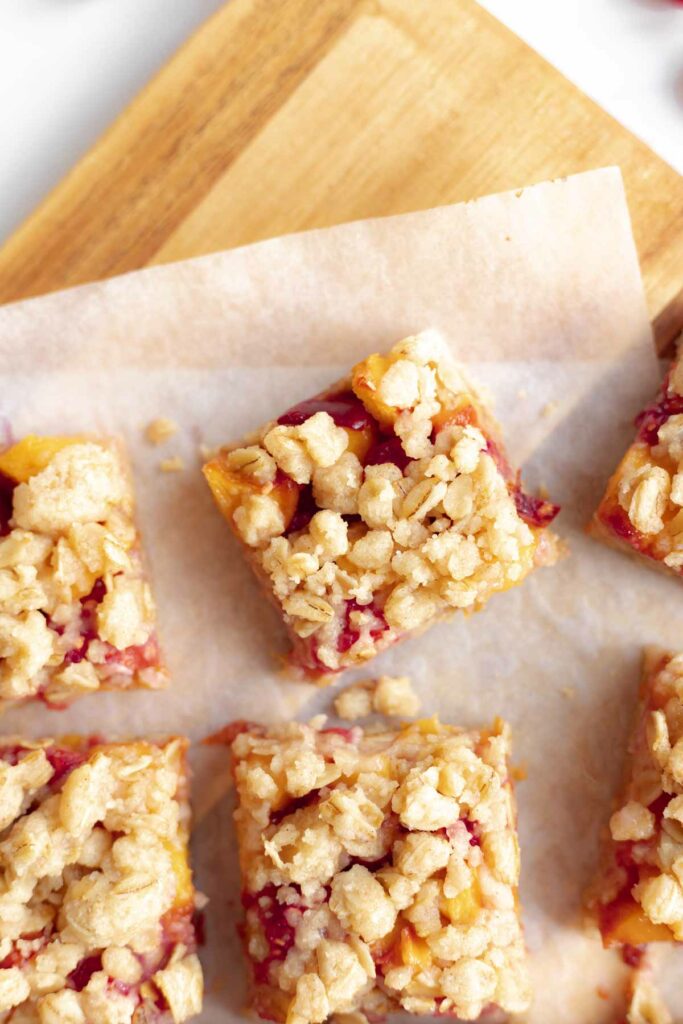 photo from above of several baked peach raspberry oat bars on a cutting board