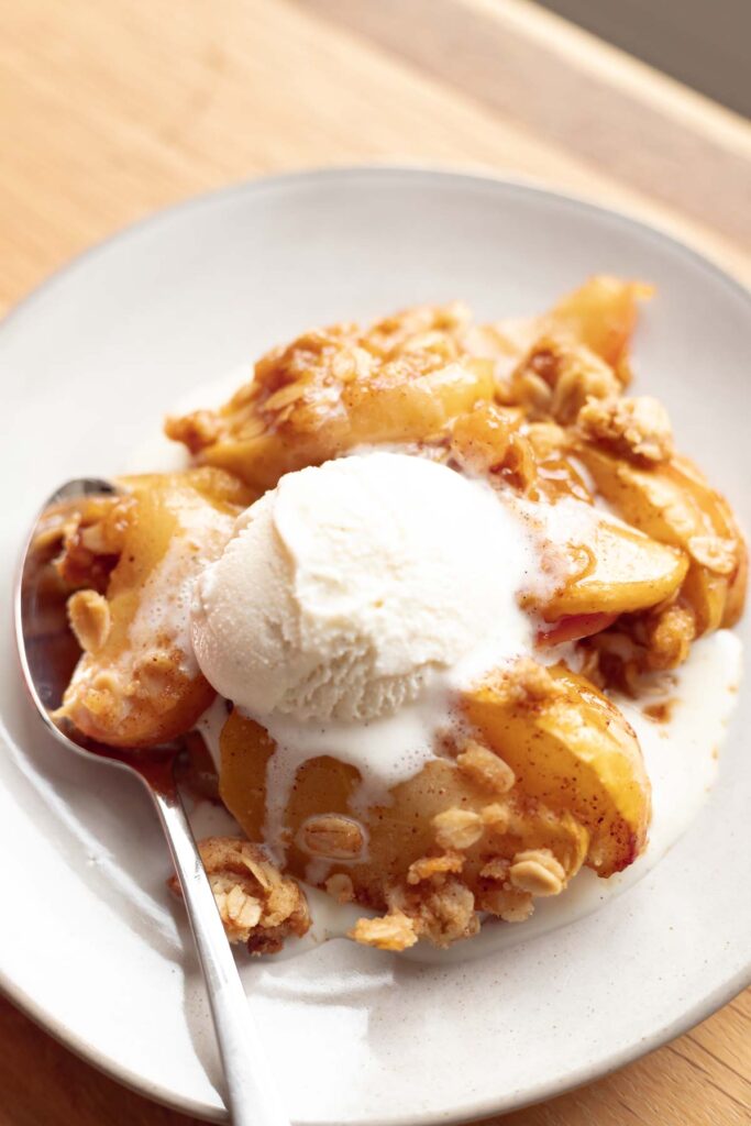 one serving of fall apple crisp in a bowl with vanilla ice cream