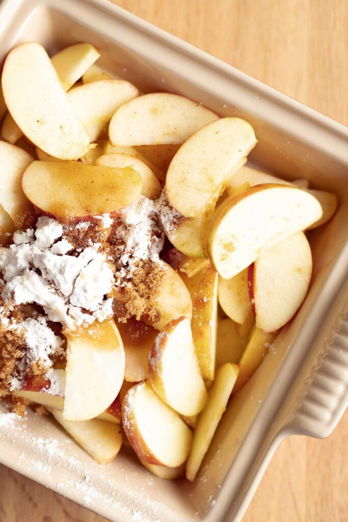 sliced apples in a baking dish layered with spices, brown sugar, and cornstarch