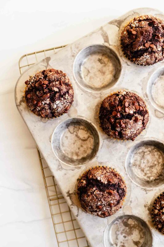 overhead view of the baked chocolate banana muffins in the muffin tin on a wire rack