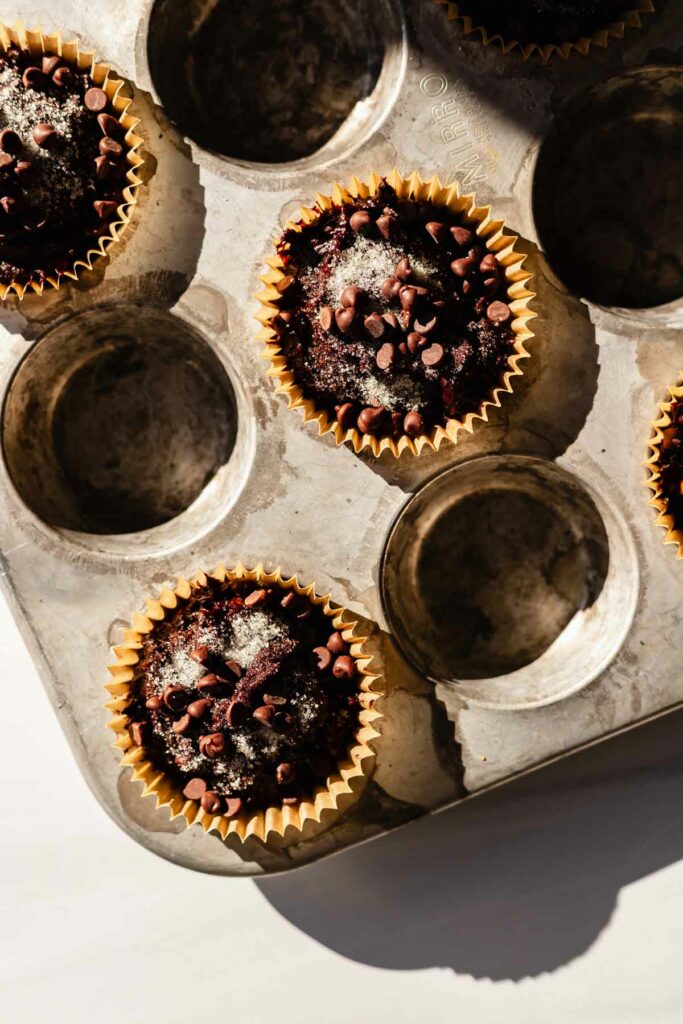 overhead view of muffin batter in every other cup of the muffin tin, in parchment paper muffin liners with extra chocolate chips sprinkled on top
