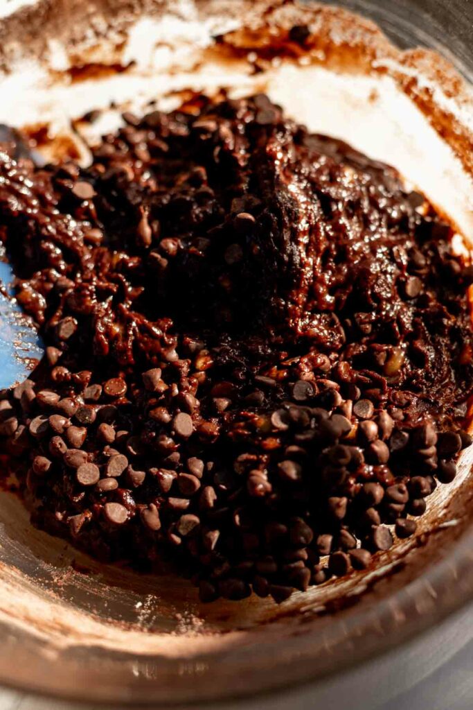 double chocolate banana muffin batter in a glass bowl with chocolate chips being stirred in