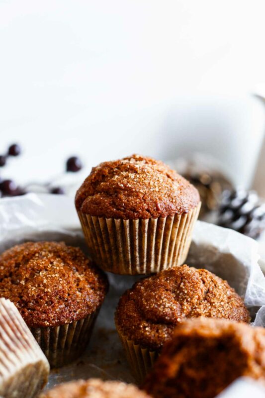 close up of a completed baked molasses muffin sitting on top of others with a white background