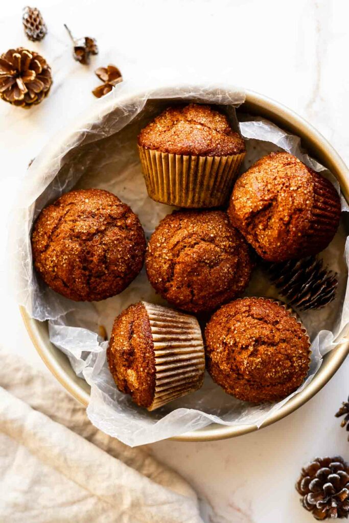 a round cake pan on a white surface containing 6 gingerbread muffins, some fallen over and some upright