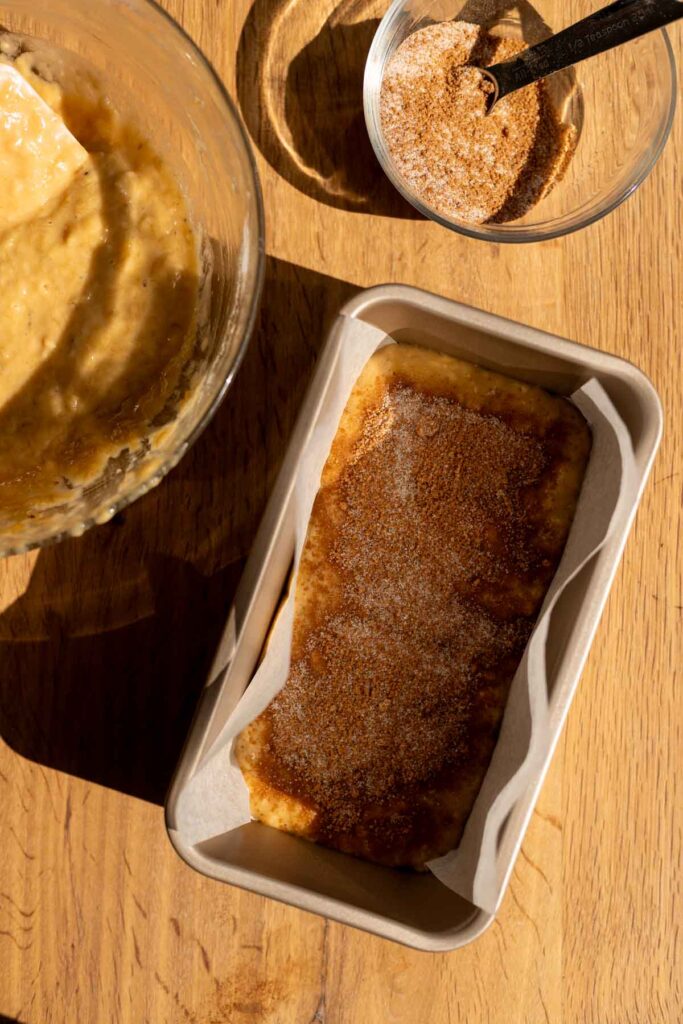 mid-preparation view, bowls and a loaf pan with half the batter in it and cinnamon sugar sprinkled on top