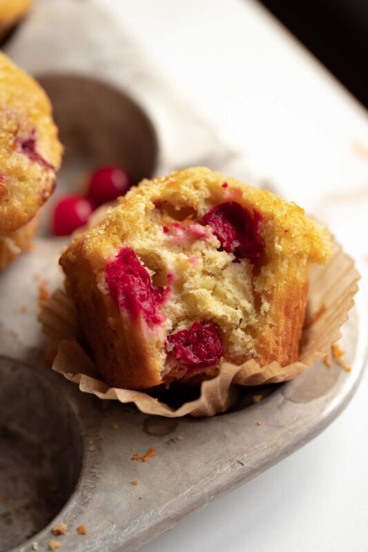 a baked muffin with a bite taken out of it to expose the soft, fluffy, and tart cranberry interior