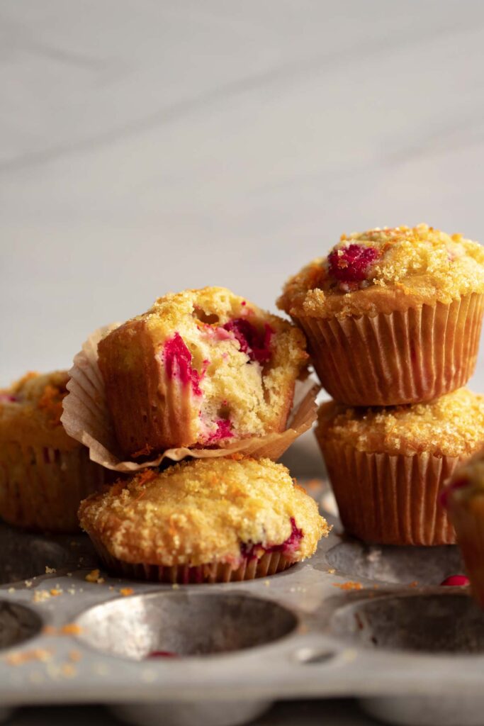 several cranberry orange muffins piled on top of each other on a muffin tin