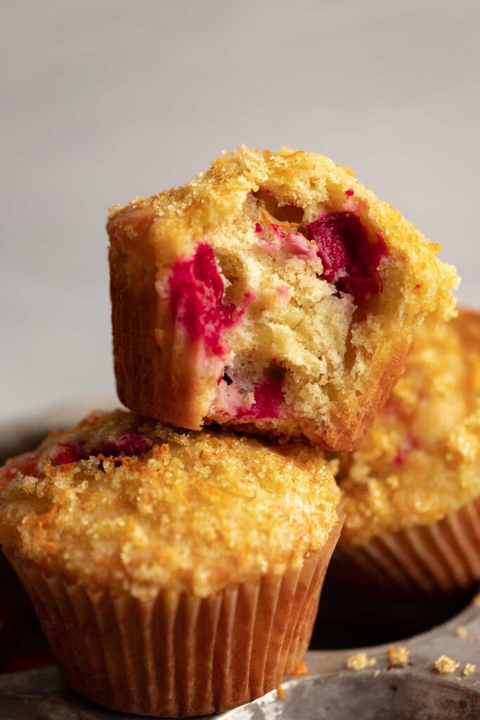 two cranberry orange muffins stacked on top of each other, one with a bite taken out of it