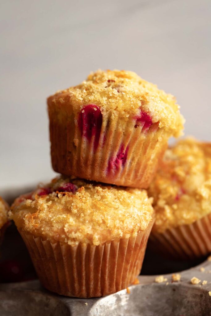 two cranberry orange muffins stacked on top of each other against a white background