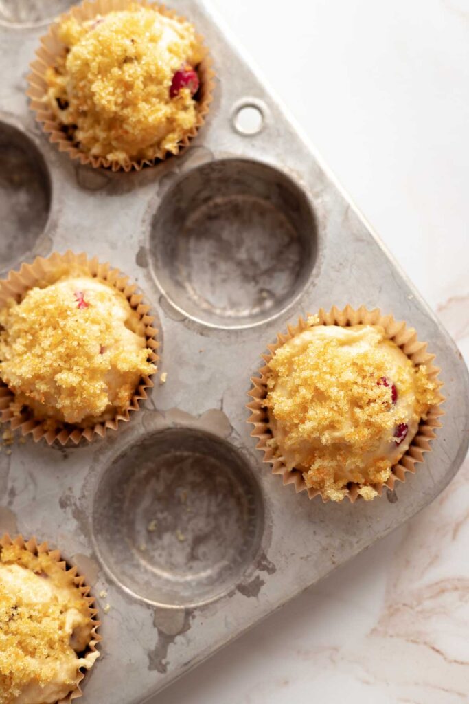 muffin batter in a muffin tin with orange sugar on top, ready to go in the oven